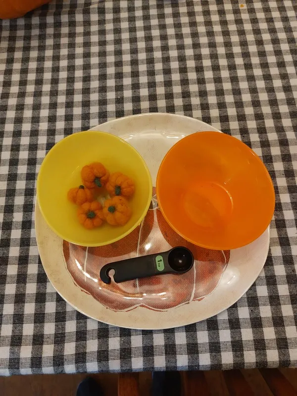 A plate with bowls, a scoop, and tiny round objects that look like pumpkins.