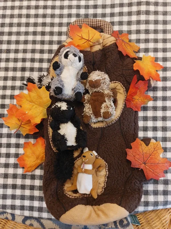 Stuffed animals lying in the holes of a plush tree with orange leaves on it.