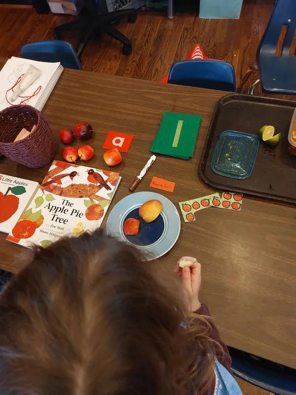 A child eating apples at a table with scattered lesson materials including books about apples.
