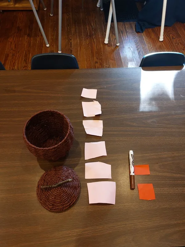 An empty basket with blank paper squares next to it and a marker.