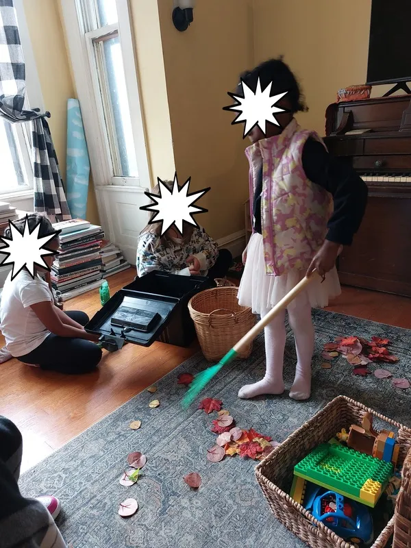 Children indoors raking play leaves into a basket.